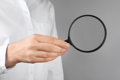 Woman holding magnifying glass on grey background, closeup. Find keywords concept