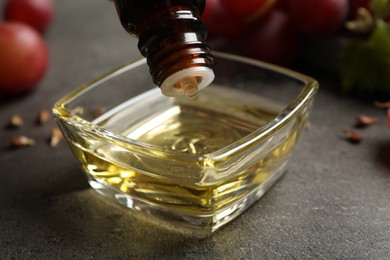 Dripping natural grape seed oil into bowl on grey table, closeup. Organic cosmetic