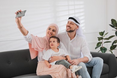 Photo of Happy Muslim family taking selfie on sofa at home