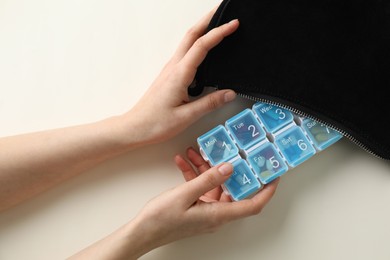 Woman putting pill box into bag on white background, top view