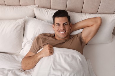 Photo of Happy man lying in bed at home, top view