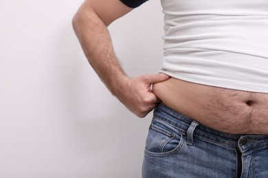 Man wearing tight t-shirt and jeans on white background, closeup. Overweight problem