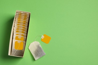 Photo of New tea bags with tabs and box on green background, flat lay. Space for text