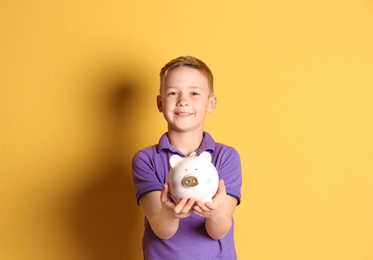 Little boy with piggy bank on color background