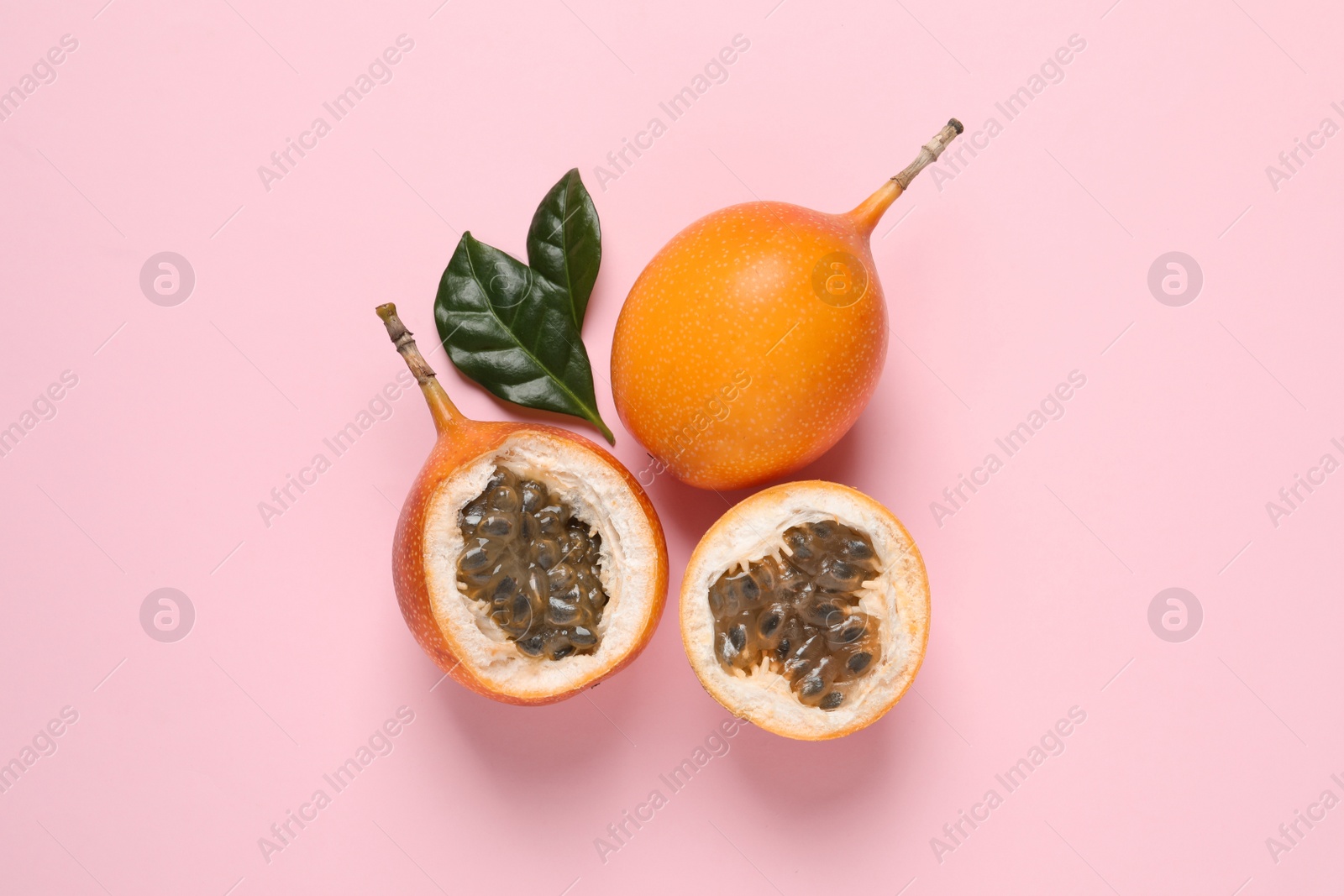Photo of Delicious ripe granadillas with leaves on pink background, flat lay