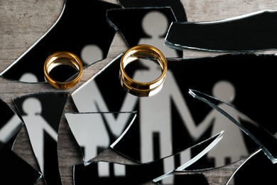 Photo of Divorce concept. Human figures reflected in broken mirror and wedding rings on wooden table