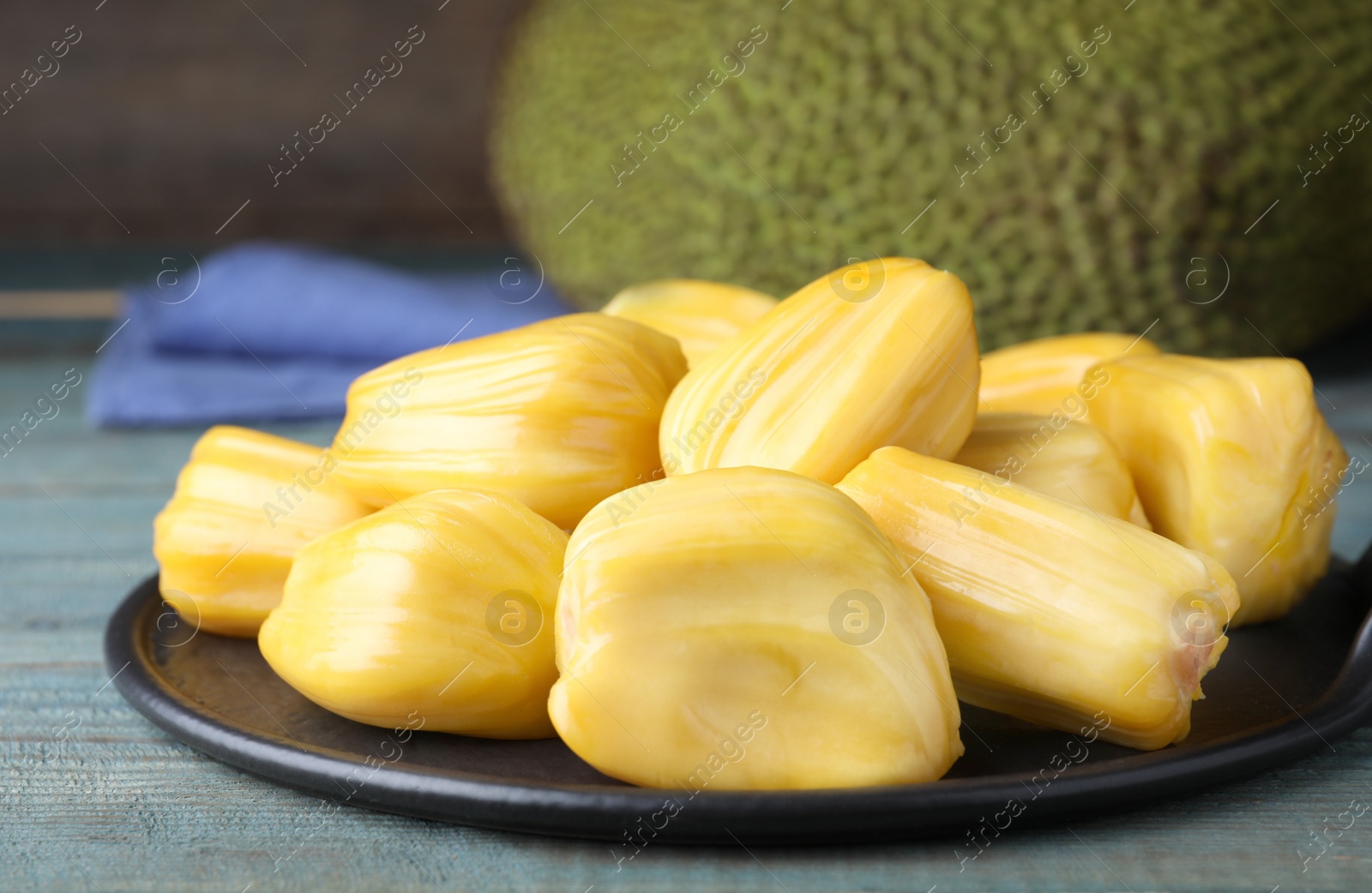 Photo of Fresh exotic jackfruit bulbs on light blue wooden table, closeup