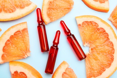 Skincare ampoules with vitamin C and slices of grapefruit on light blue background, flat lay