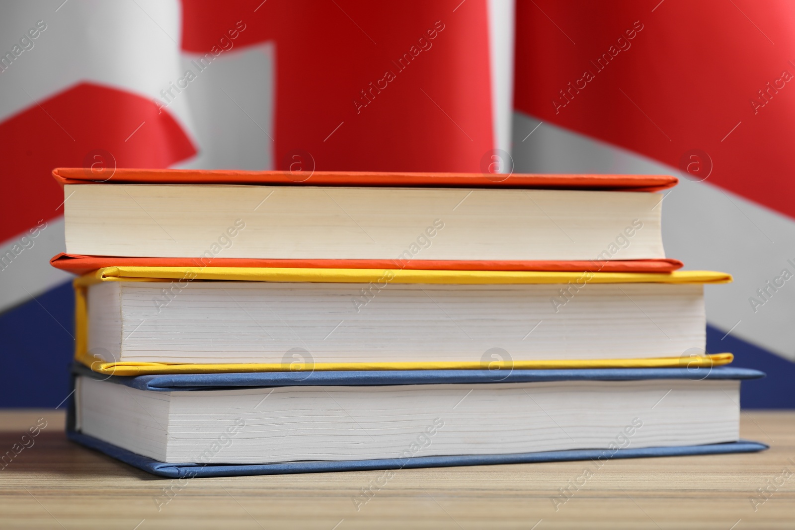 Photo of Learning foreign language. Different books on wooden table near flag of United Kingdom, closeup