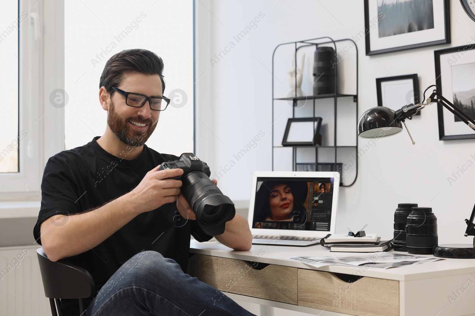 Photo of Professional photographer in glasses holding digital camera at table in office