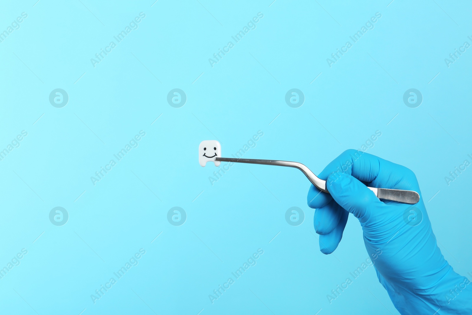 Photo of Dentist holding small plastic tooth with tweezers on color background. Space for text