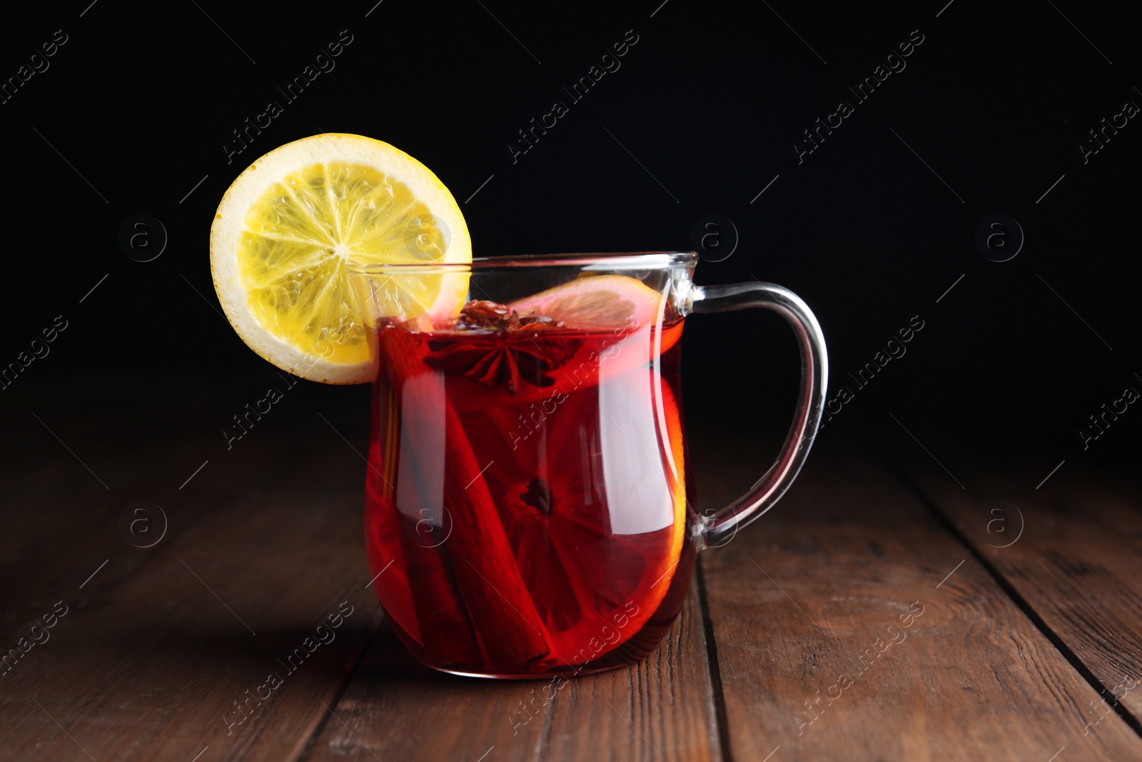Photo of Cup with red mulled wine on wooden table against dark background
