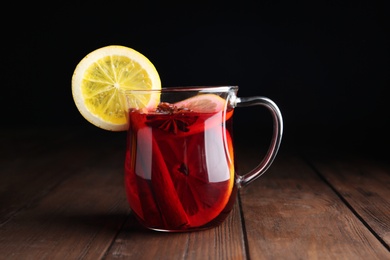 Photo of Cup with red mulled wine on wooden table against dark background