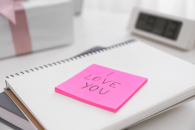 Photo of Memory sticker with phrase I Love You on notebook at table, closeup. Valentine's Day celebration