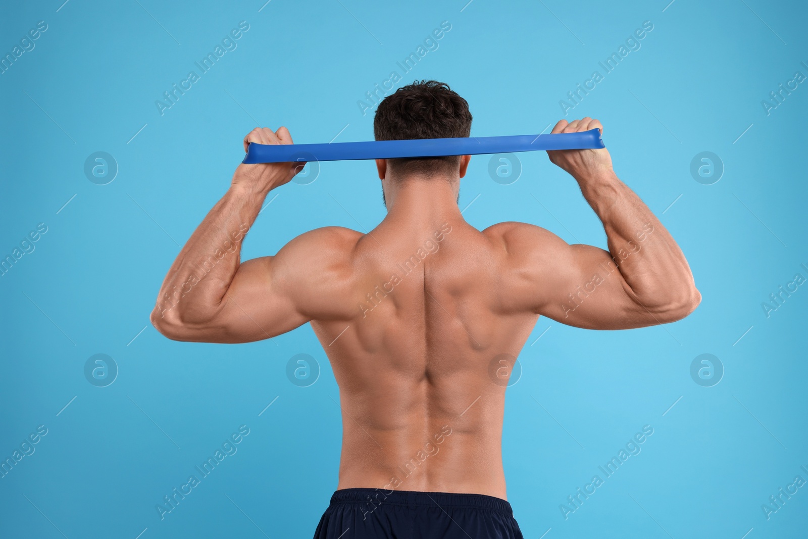 Photo of Young man exercising with elastic resistance band on light blue background, back view