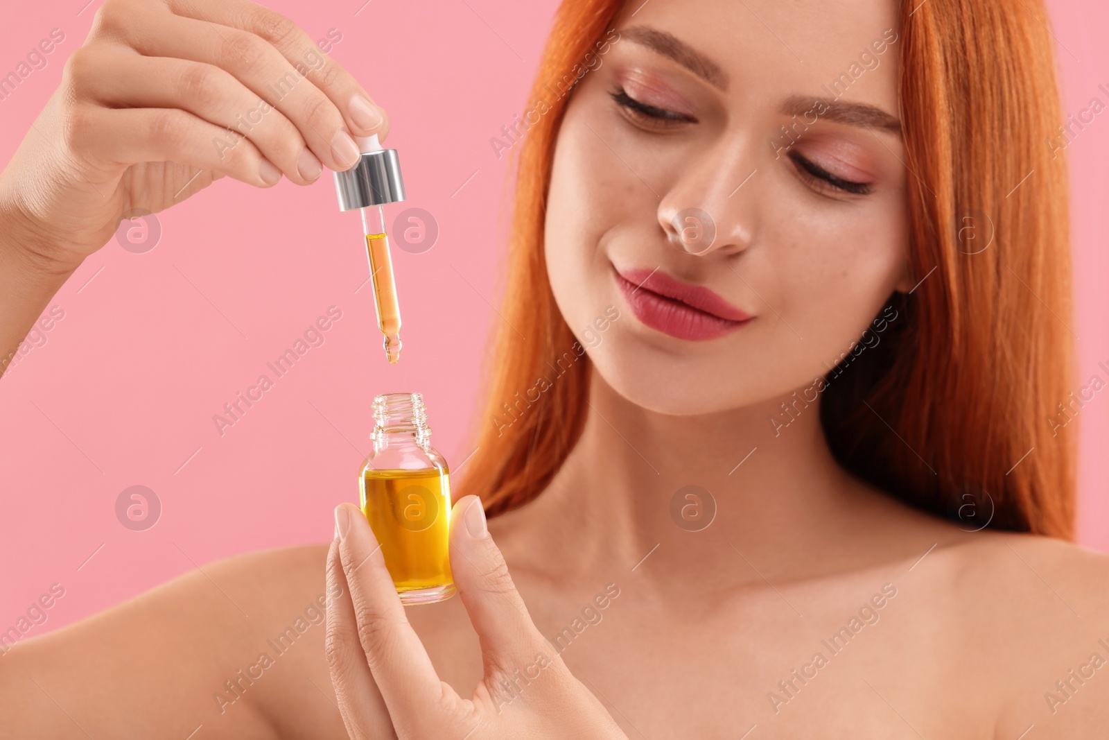 Photo of Beautiful young woman with bottle of cosmetic serum on pink background, closeup