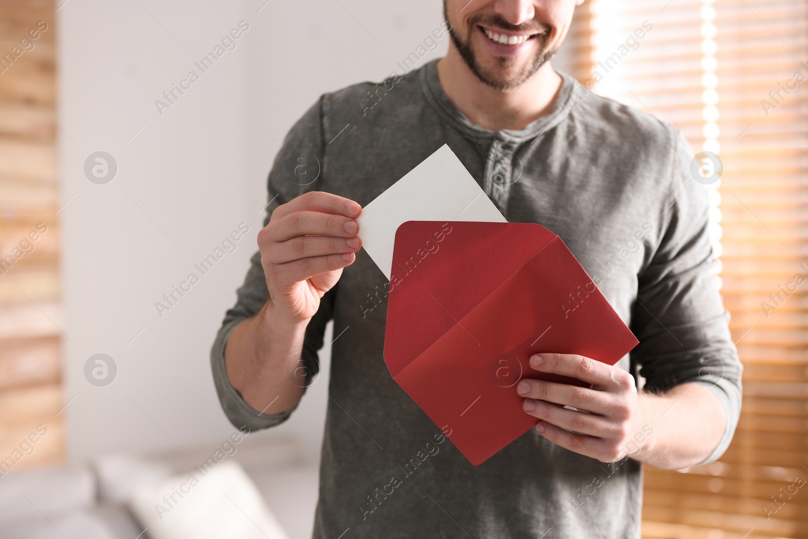 Photo of Man holding envelope with blank greeting card indoors. closeup