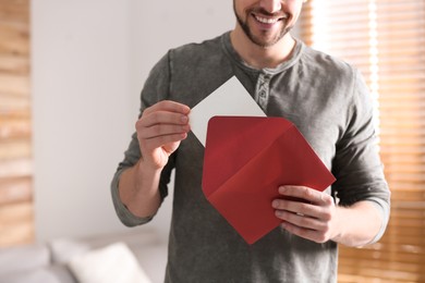 Photo of Man holding envelope with blank greeting card indoors. closeup