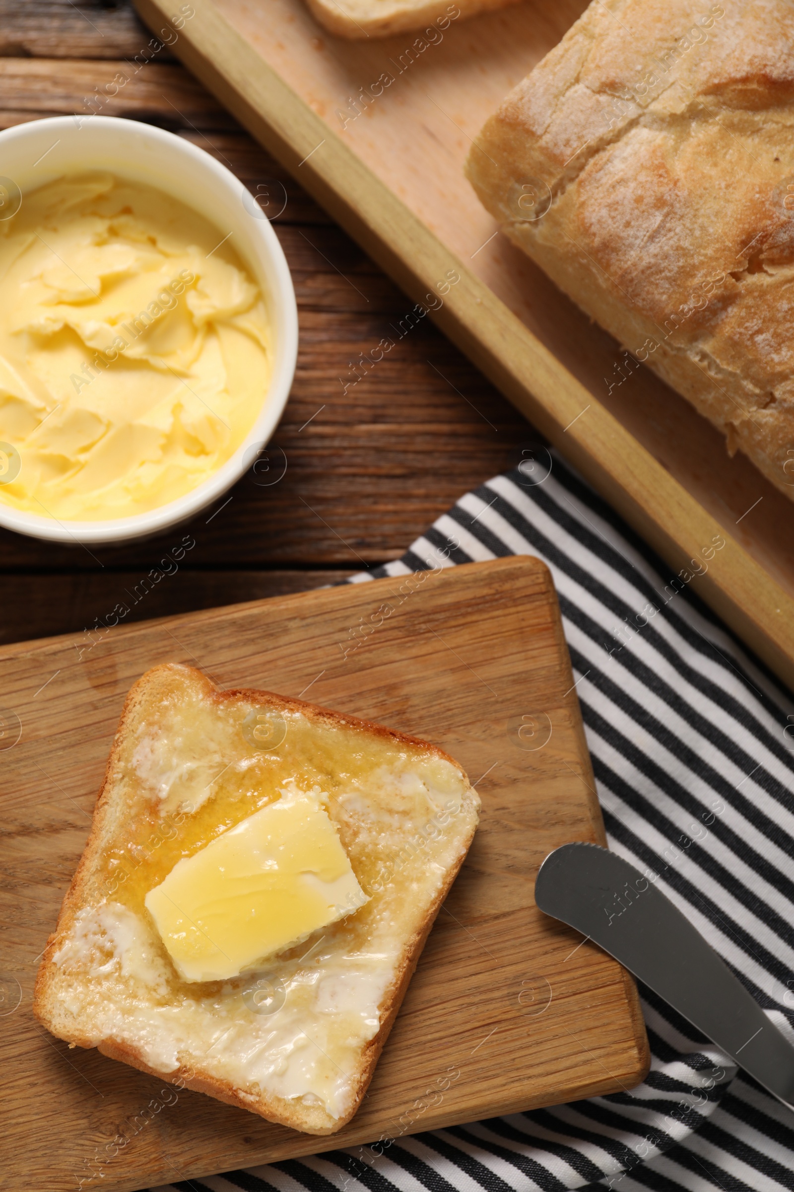 Photo of Melting butter, toast and knife on wooden table, top view