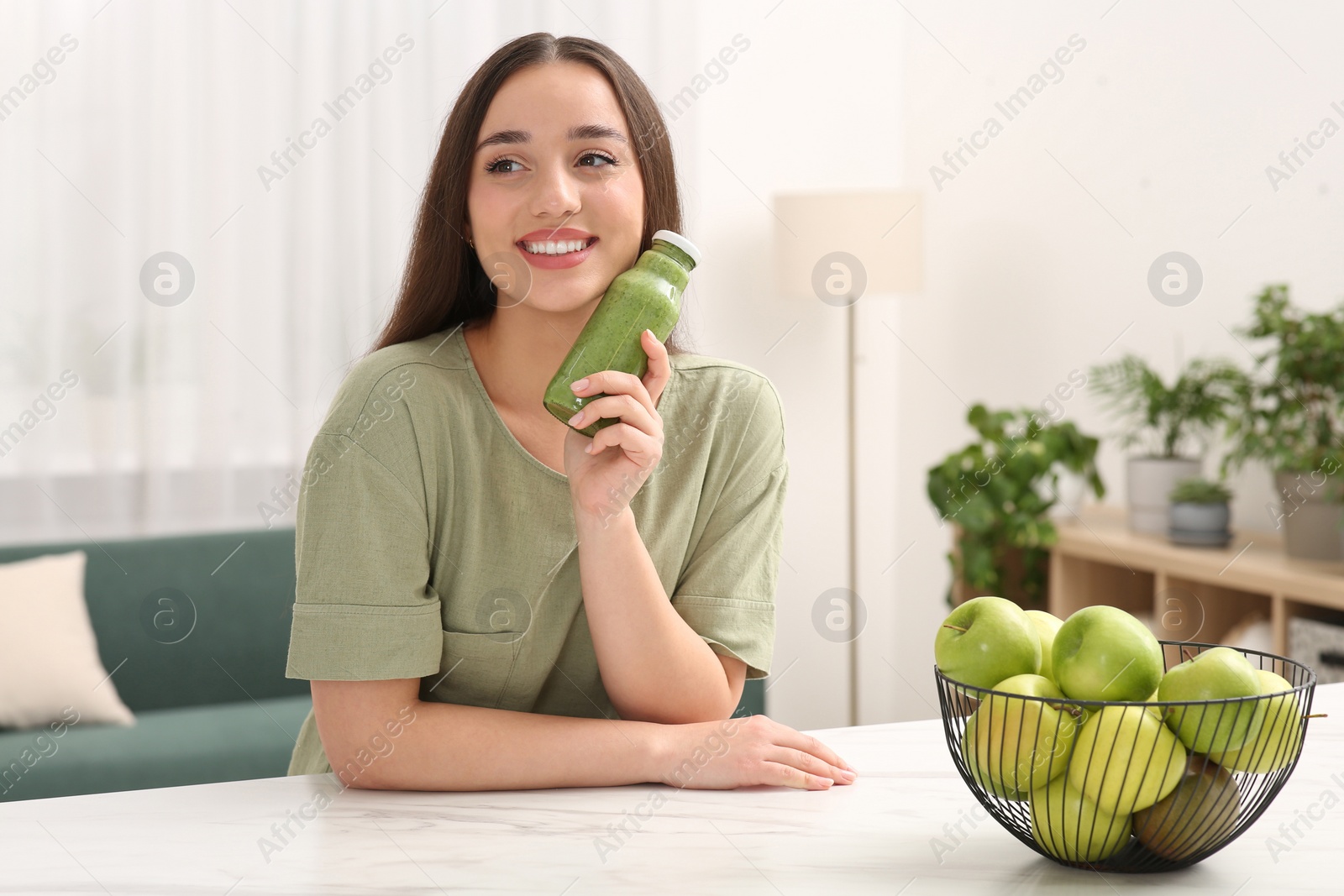 Photo of Beautiful woman with bottle of delicious smoothie at table indoors