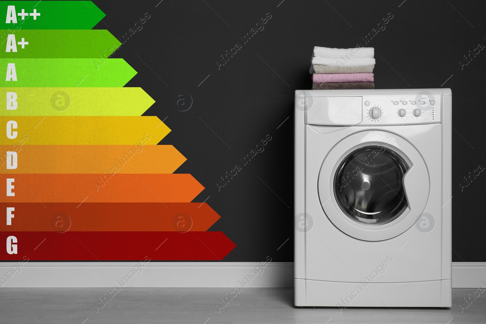 Image of Energy efficiency rating label and washing machine with laundry near black wall indoors