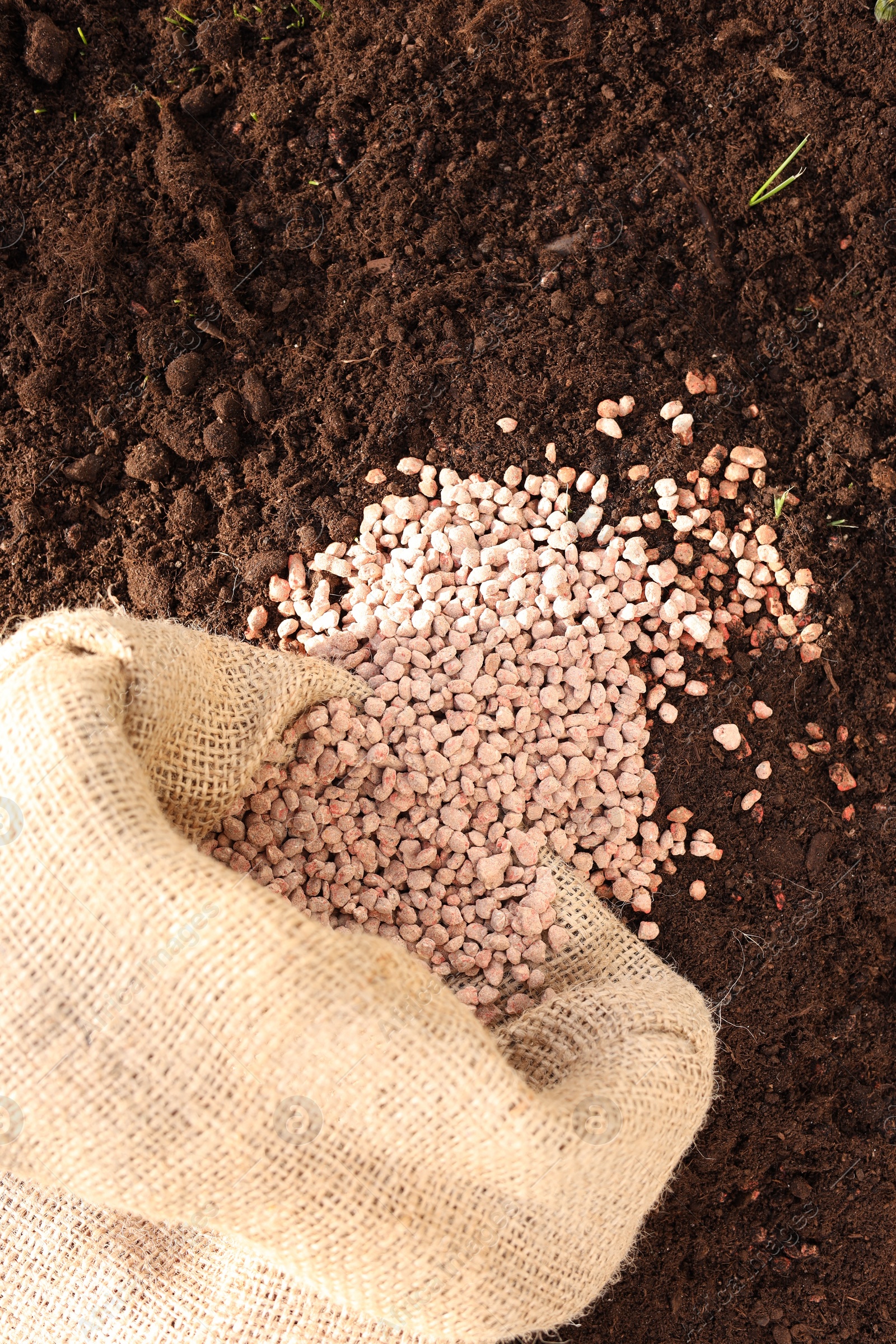 Photo of Granulated fertilizer in sack on soil, top view