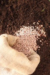 Granulated fertilizer in sack on soil, top view