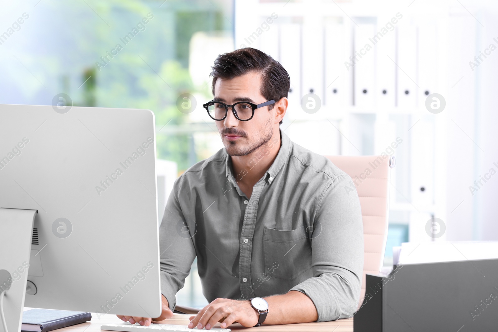 Photo of Handsome young man working with computer at table in office