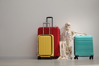 Waiting concept. Human skeleton with suitcases near light grey wall, space for text