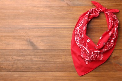 Photo of Tied red bandana with paisley pattern on wooden table, top view. Space for text