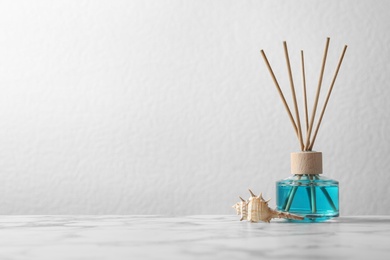 Photo of Aromatic reed freshener and sea shell on marble table against light background, space for text