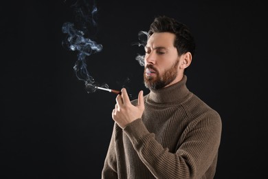 Man using cigarette holder for smoking on black background, space for text