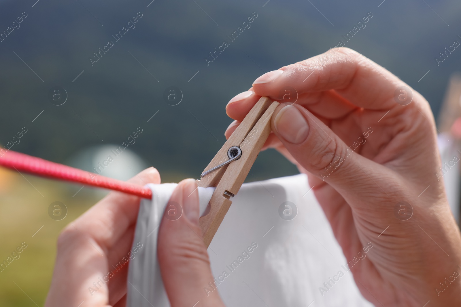 Photo of Woman hanging clean laundry with clothespin on washing line outdoors, closeup