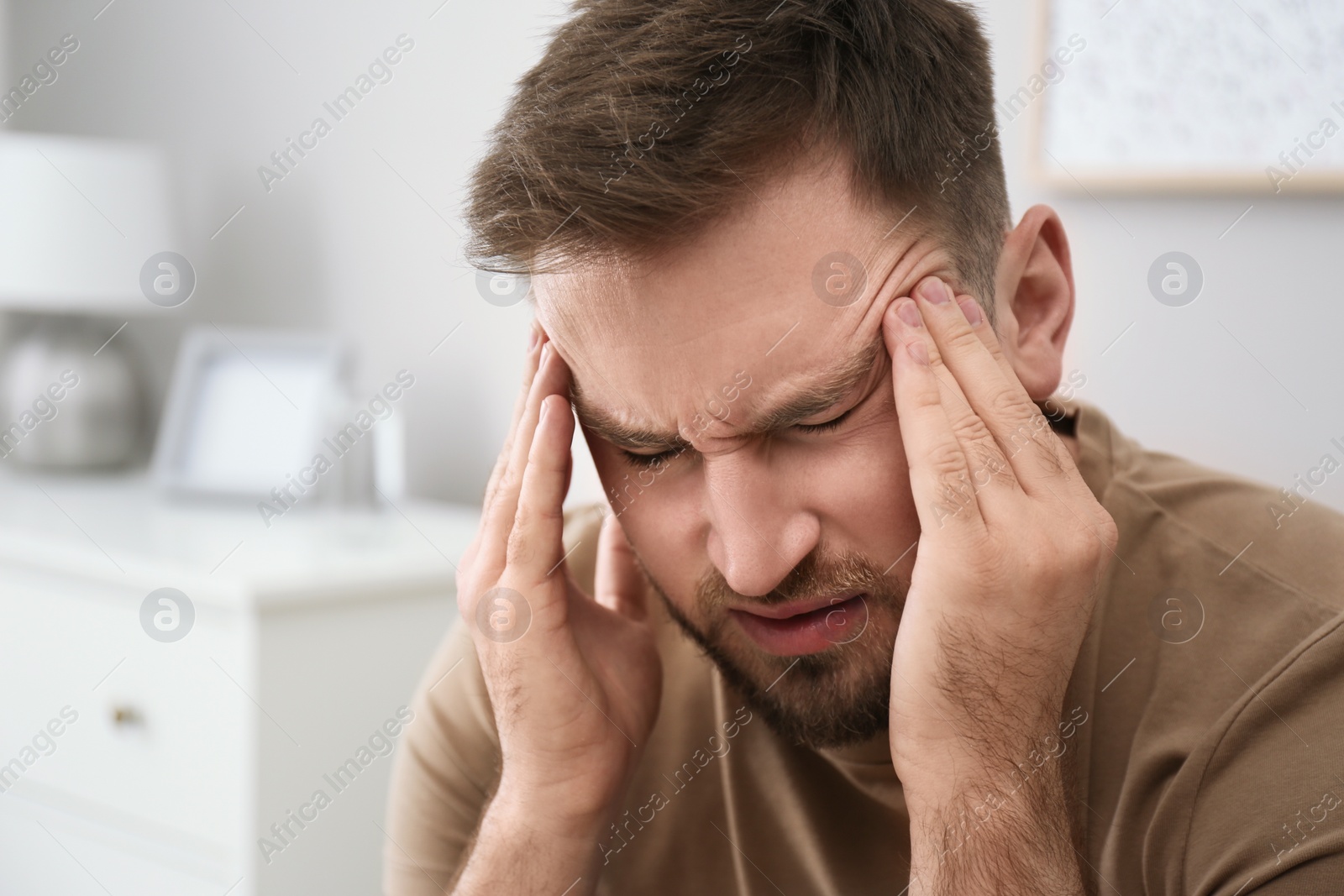 Photo of Young man suffering from migraine at home, closeup