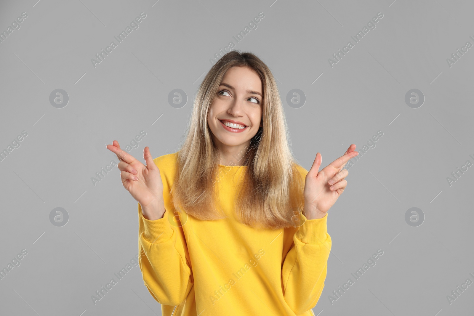 Photo of Woman with crossed fingers on light grey background. Superstition concept