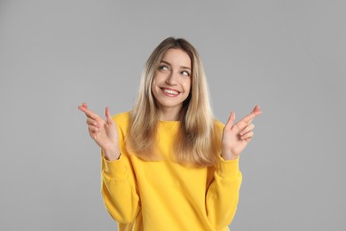 Photo of Woman with crossed fingers on light grey background. Superstition concept