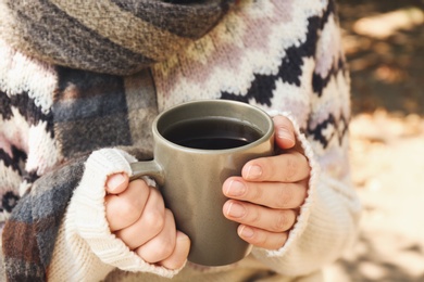 Photo of Woman in cozy sweater with cup of hot drink outdoors on sunny autumn day, closeup