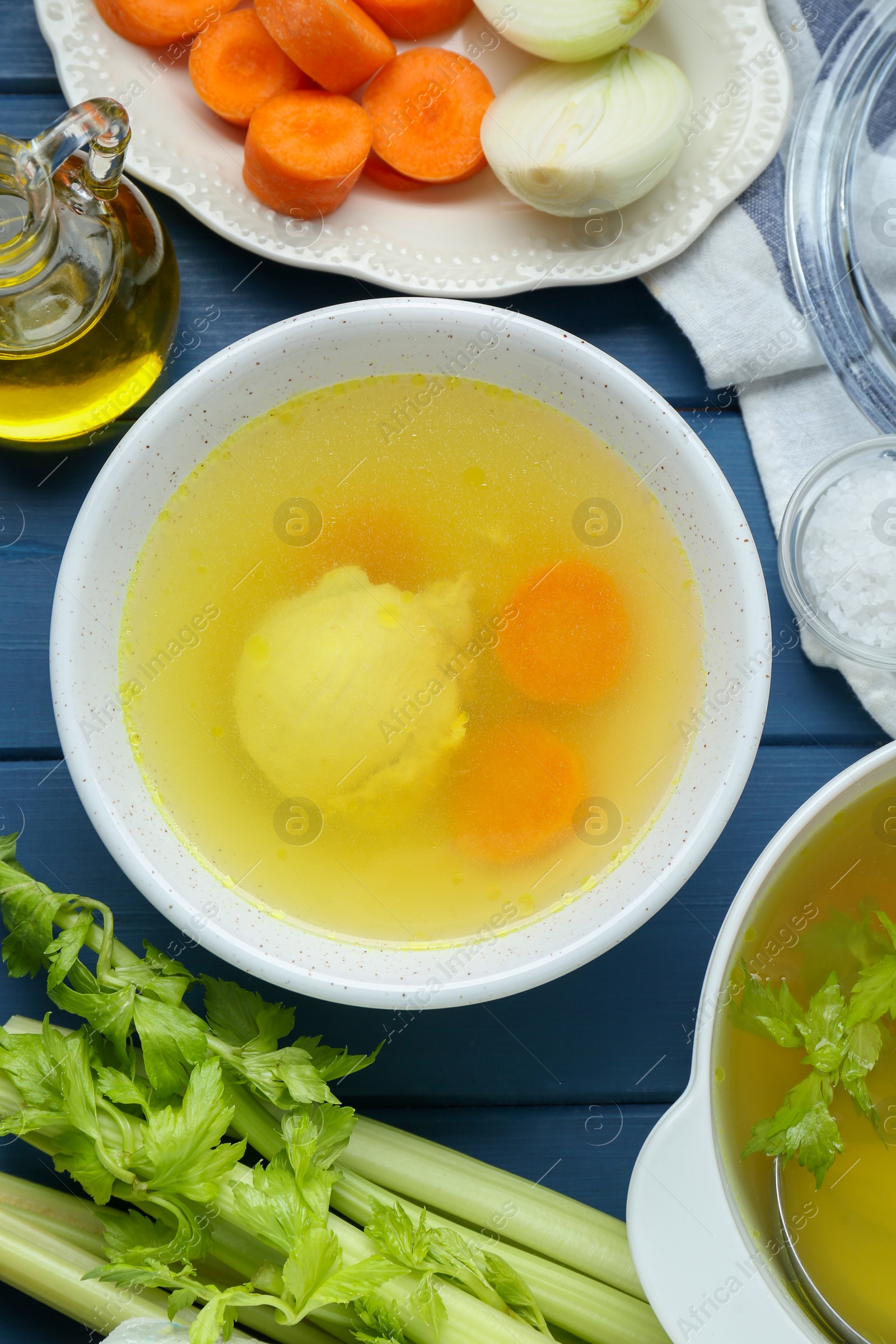 Photo of Delicious chicken bouillon and ingredients on blue wooden table, flat lay