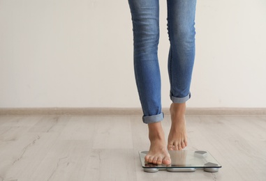 Woman measuring her weight using scales on wooden floor. Healthy diet