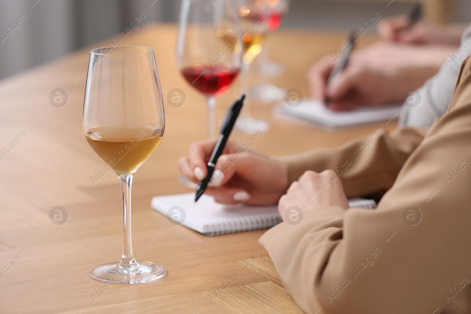 Photo of Sommeliers making notes during wine tasting at table indoors, closeup