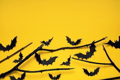 Photo of Flat lay composition with black branches and paper bats on yellow background, space for text. Halloween celebration