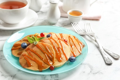 Tasty pancakes with berries and syrup on table