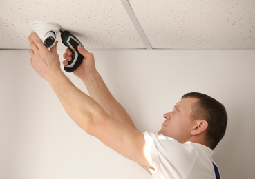 Technician installing CCTV camera on ceiling indoors