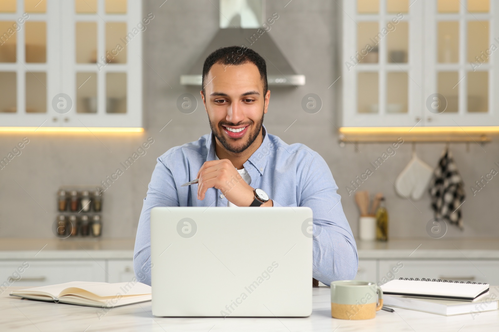 Photo of Young man working on laptop at desk in kitchen. Home office