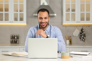 Photo of Young man working on laptop at desk in kitchen. Home office