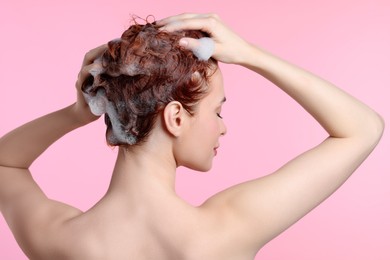 Photo of Young woman washing her hair with shampoo on pink background, back view