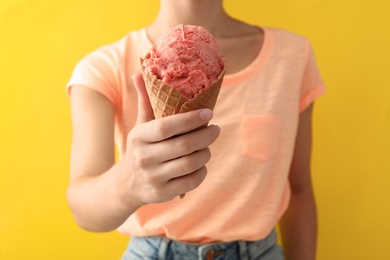 Woman holding pink ice cream in wafer cone on yellow background, closeup