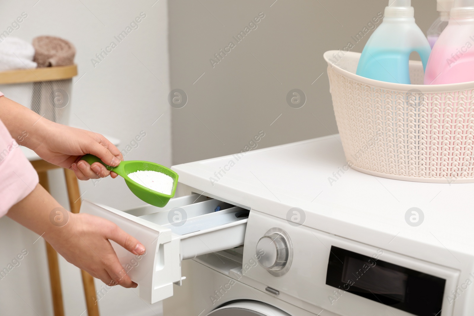 Photo of Woman pouring powder into drawer of washing machine in laundry room, closeup