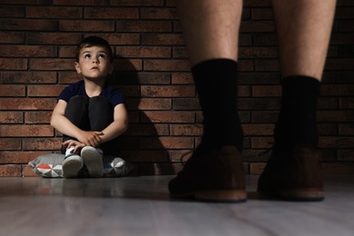 Photo of Adult man without pants standing in front of despaired little boy indoors. Child in danger