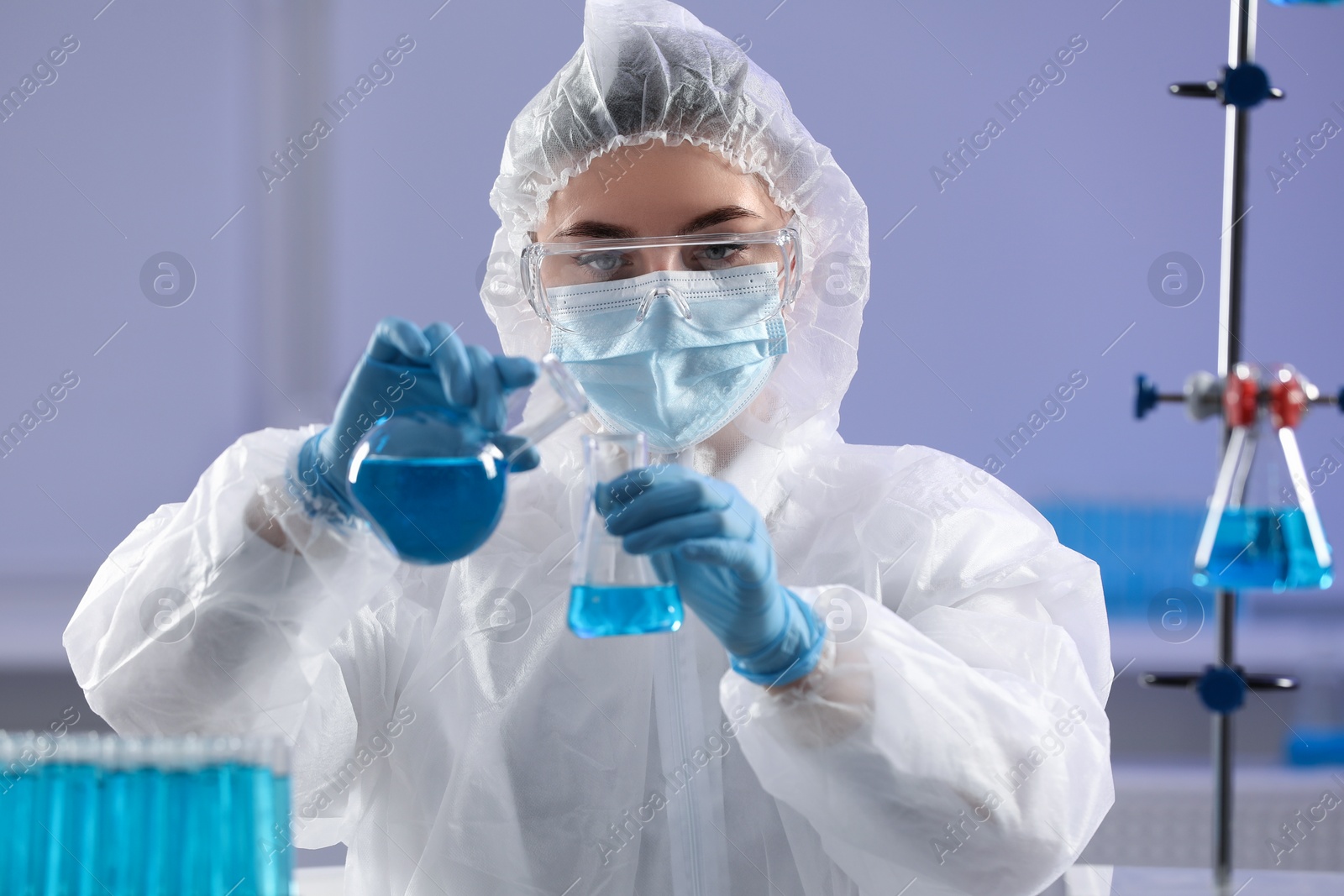 Photo of Scientist holding flasks with light blue liquid in laboratory